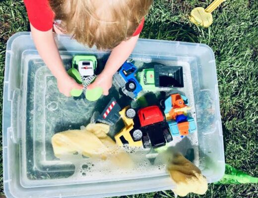 Toddler enjoying a simple indoor sensory water play activity with toy trucks and soap