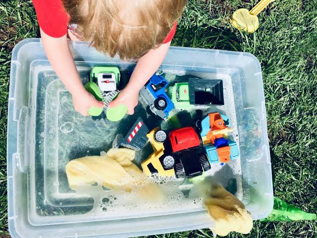 Toddler enjoying a simple indoor sensory water play activity with toy trucks and soap